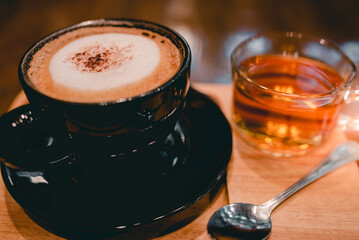 Hot Cappuccino Coffee in a Cup of Black Fresh Coffee With a cup of tea beside each other Beautiful places in a coffee shop The background is a brown wooden table.