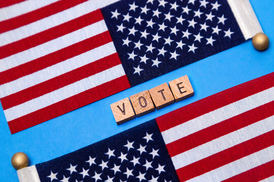 Two American Flags with the  signs wooden letter VOTE  in the light blue background