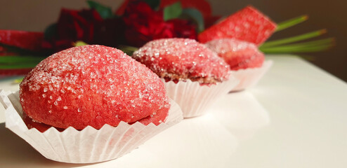 Red round Italian cookies on a background of red roses in the morning sun. Flowers and sweetness for love.