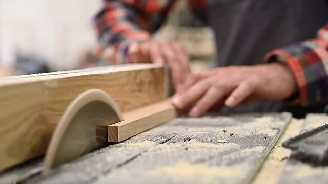 Working process in the carpentry workshop.A man in overalls works in a carpentry workshop.Carpenter using sawing machine for cutting wooden board at sawmill.Profession, carpentry, woodwork concept