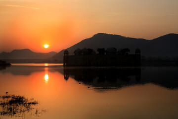 A view of Sunrise.Sun rising from behind the Hills and showing its reflection in the water of the lake. 