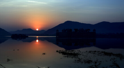 A view of Sunrise.Sun rising from behind the Hills and showing its reflection in the water of the lake. 