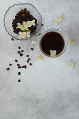 Obraz na płótnie Canvas Coffee beans and cup of black coffee and white spring flowers top view. Copy space for text