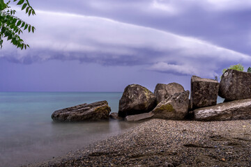 Nuages d'orage en bord de plage et devant des rochers sur le lac Léman