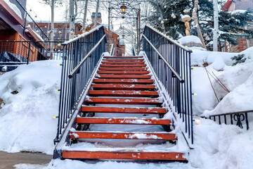 Stairs against snow covered slope with houses and trees under cloudy winter sky