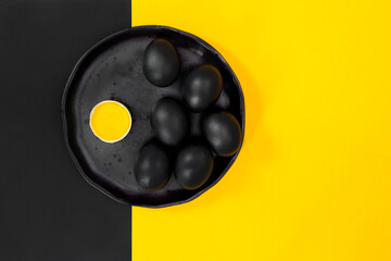 Black eggs on a black plate with a crashed egg on a flat black background with yellow, pop art.