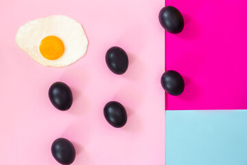 Six whole black eggs on pink with blue background with one fried egg, pop art.