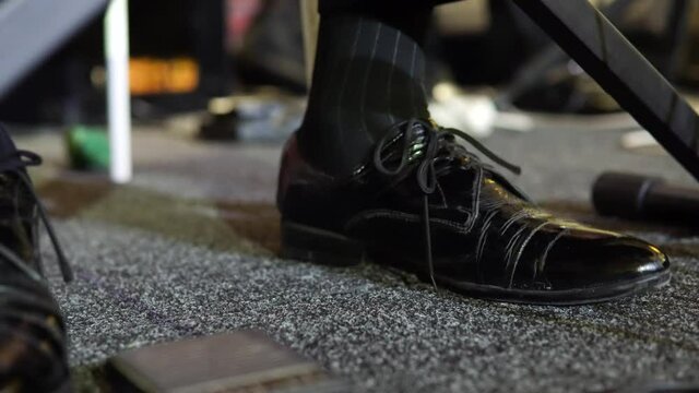 The foot of the musician stomps to the beat of the music. A man in shoes beats the beat to the music. Close-up.