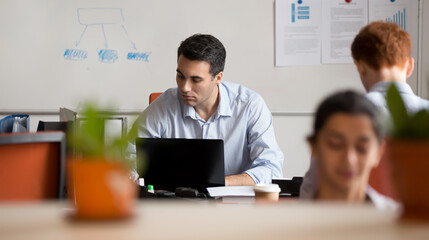 Serious busy businessman employee working on laptop in coworking space with colleagues, looking at computer screen, using software, writing report or analyzing project statistics, horizontal photo