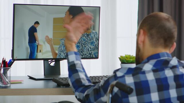 Guy in wheelchair waving at friends during a video call. Handicapped invalid paralysed freelancer, immobilized entrepreneur working from home, ilness and disability