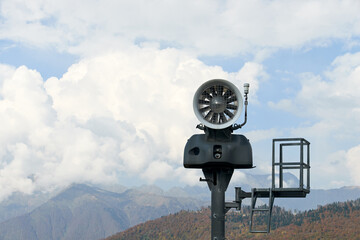 Nature landscape and travel concept. Snow cannon in mountains against the blue sky with clouds in early autumn