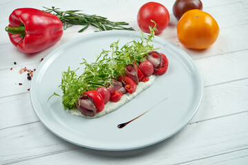 Delicious salad with roast beef, baked tomatoes and pepper with garlic sauce in a white plate on a wooden background