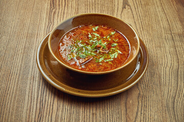 Classical Georgian soup red Kharcho with tomatoes and spices in a ceramic plate on a wooden background