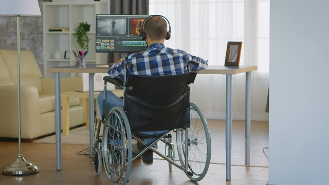 Videographer with headphones and moving handicap sitting on wheelchair working on movie. Handicapped invalid paralysed freelancer, immobilized entrepreneur working from home, ilness and disability