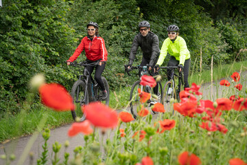 Grandmother, son and granddaughter ridung their bicycles on a weekend trip with blooming flowers alongside the bike lane 