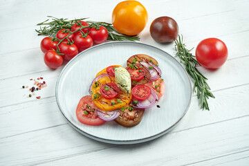 Delicious vegetarian salad of 3 types tomatoes, onions and sauce in a grey plate on a wooden background