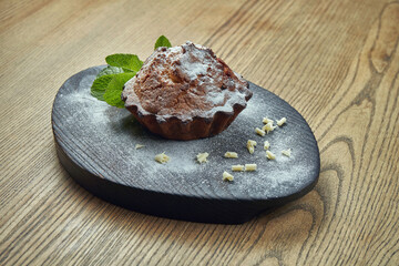 Homemade pastry - chocolate muffin with mint and nuts on a black tray on a wooden background