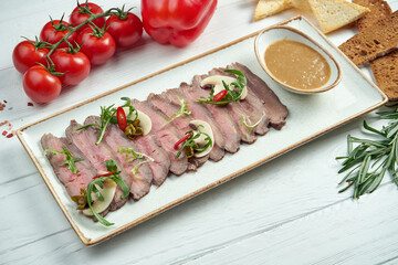 Roast beef with fresh mushrooms, nut sauce and capers in a white plate on a wooden background.