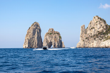 Fototapeta na wymiar The blue sea and the faraglioni of Capri with a yacht in the foreground. Summer mood in Italy