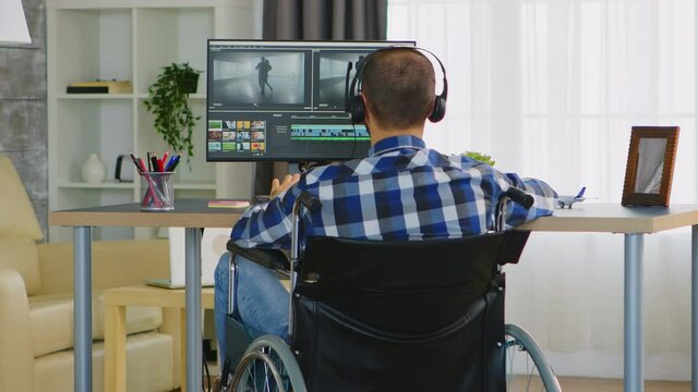 Videographer with handicap sitting on wheelchair doing color grading on film. Wearing headphones. Handicapped invalid paralysed freelancer, immobilized entrepreneur working from home, ilness