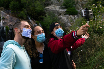 Caucasian people taking a selfie wearing mask in a waterfall. Group of people travelling around Europe during the coronavirus (covid 19) health crisis wearing sanitary mask. Eco turism