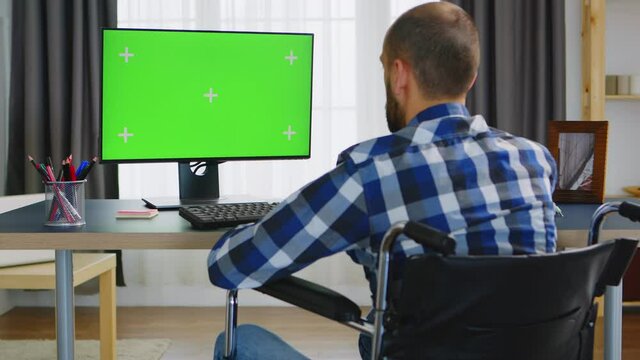 Invalid man in wheelchair working on computer with green screen. Handicapped invalid paralysed freelancer, immobilized entrepreneur working from home, ilness and disability