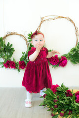 Little cute girl 1 year old in a dress of Marsala color with a wicker basket with peonies. Spring and flowers. Children's fashion
