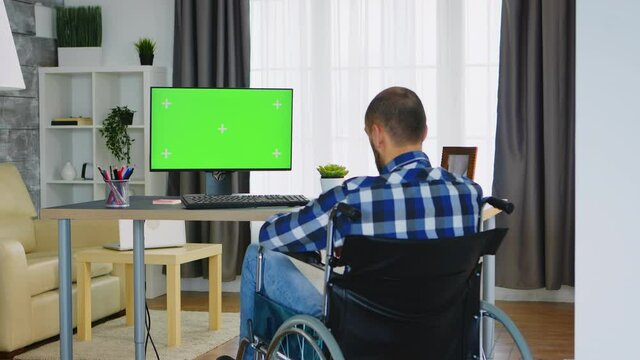 Invalid man in wheelchair working on computer with green screen. Handicapped invalid paralysed freelancer, immobilized entrepreneur working from home, ilness and disability