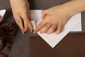 Origami is the ancient art of folding paper. Female hands make a figure on a cozy brown background with lights and a warm lamp