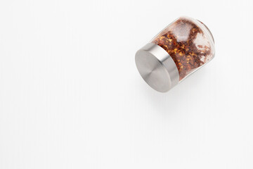 Jar of hot red pepper seasoning on white wooden background with copyspace