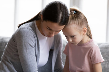 Close up caring young mother calming comforting offended little daughter, touching foreheads,...