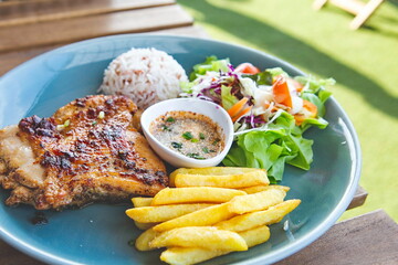 Grilled chicken, french fries, salad and rice in a high angle dish