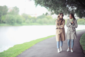Fototapeta na wymiar autumn fashion park girls two look / walk in a city park two glamorous fashionable girlfriends in a coat