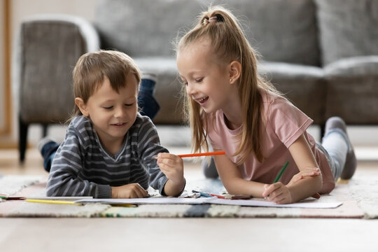 Happy little girl and boy drawing with colorful pencils in album at home, preschool sister and brother enjoying leisure time, playing together on warm floor with underfloor heating in living room