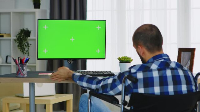 Man with disabilities sitting on wheelchair working on computer in his apartment. Handicapped invalid paralysed freelancer, immobilized entrepreneur working from home, ilness and disability