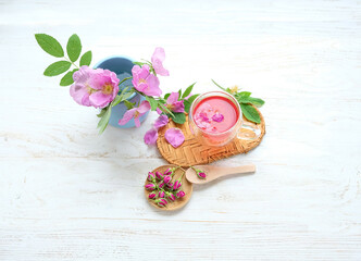 cup of tea with hip roses on wooden white table. healthy tea with wild rose and blooming rose flowers. copy space