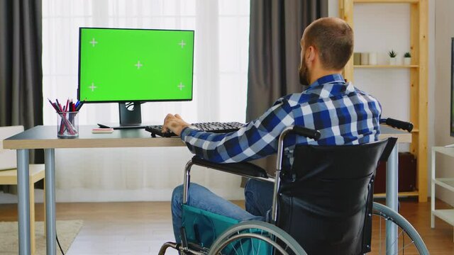 Freelancer in wheelchair typing on computer with green screen from home office. Handicapped invalid paralysed freelancer, immobilized entrepreneur working from home, ilness and disability