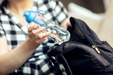 Woman takes the bottle out from backpack. Woman takes the reusable bottle of fresh water with carbon filter out from her backpack. - obrazy, fototapety, plakaty