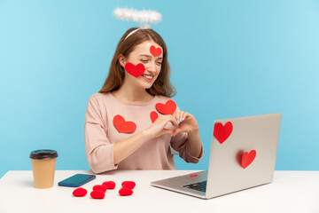 Attractive angelic woman with kind expression sitting covered with sticker love hearts, showing...