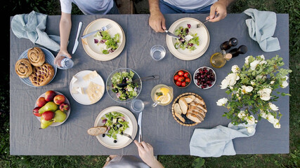 Family dinner outdoors. Family dinner with organic salad and cheese on trendy scandinavian style table in garden. Healthy aesthetic beautiful food, summer staycation concept. Aerial view or top view