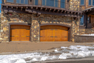 Fototapeta na wymiar facade of home featuring two hinged wooden garage doors and stone brick wall