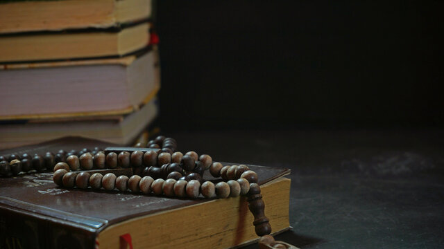 Quran the holy book of muslims and prayer beads with stack of books background