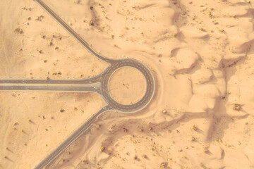 Aerial view of a road and roundabout crossing in the middle of a sandy desert in afternoon light.