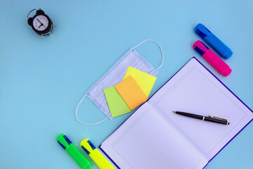 notebook, pen, note paper, alarm clock, face mask on a blue background, back to school