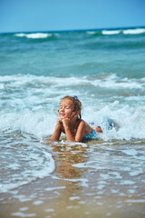 Happy little girl lies on the seashore in the waves