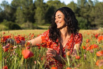 Woman in red dress touching flowers with happy expression in the middle of a poppy field