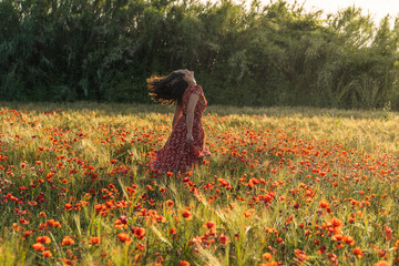 Woman in red dress running in the middle of a poppy field
