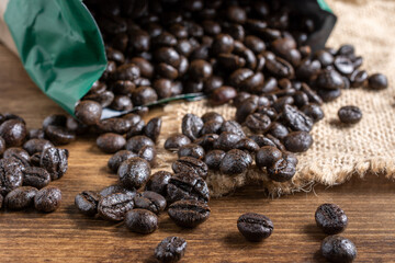 Top view of coffee beans coming out of a bag on burlap and wooden table, horizontal