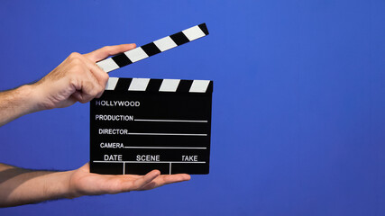 hand holding movie clapper board on blue background
