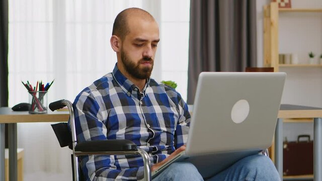 Handicapped freelancer in living room in wheelchair working on laptop. Handicapped invalid paralysed freelancer, immobilized entrepreneur working from home, ilness and disability